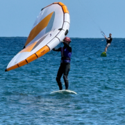 Person auf Surfbrett beim Kitesurfen mit zweiter Person im Hintergrund. Treutlein in Kooperation mit Wing Club World.